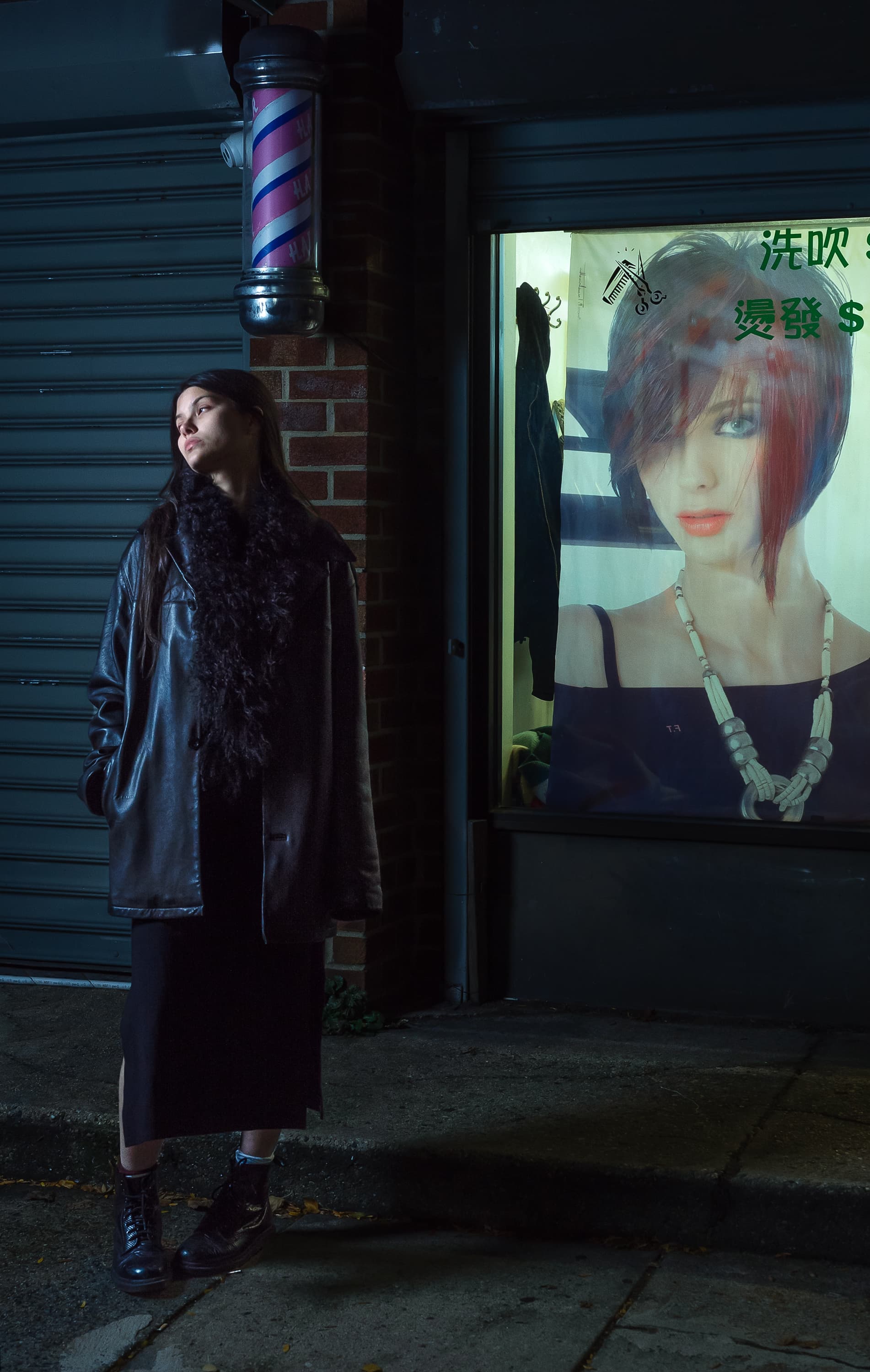 어두운 거리, 불 켜진 포스터 옆에 선 긴 코트 차림의 여자
